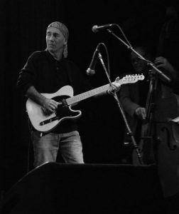Jim playing electric guitar on stage, black and white.